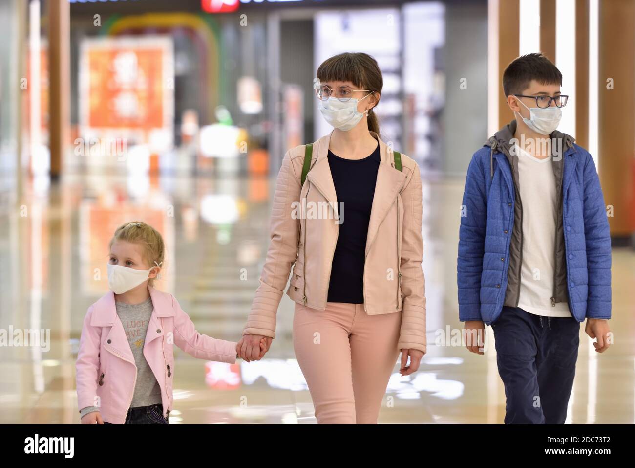 Young mother with her daughter and son in protective masks are walking along the mall Stock Photo