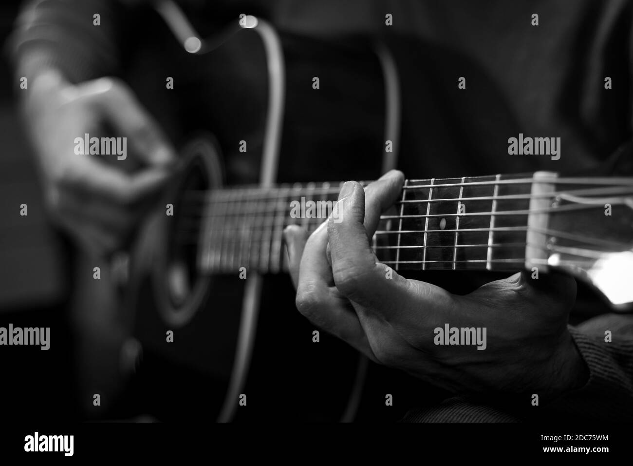 Close up view of hands playing acoustic western guitar. Black and white image. Stock Photo