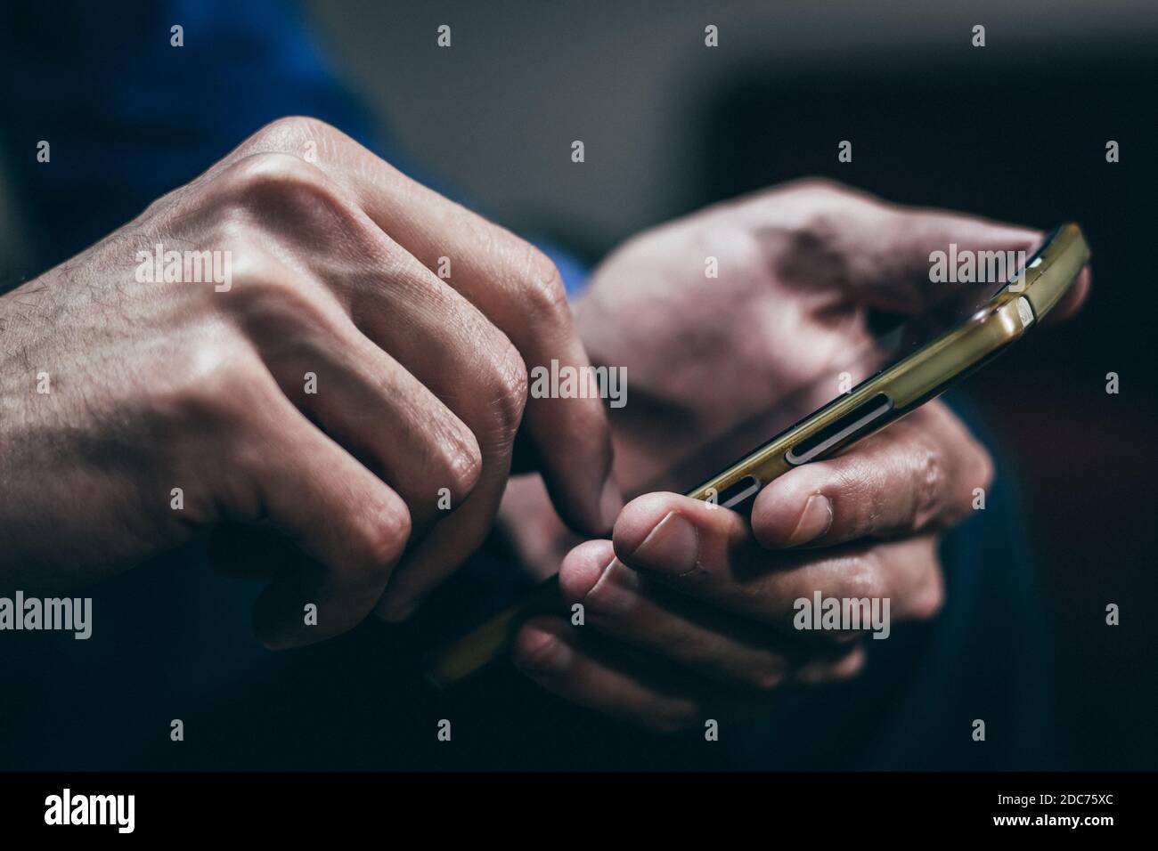 Man holding and using a smartphone with both hands. Close up, dark tone ...