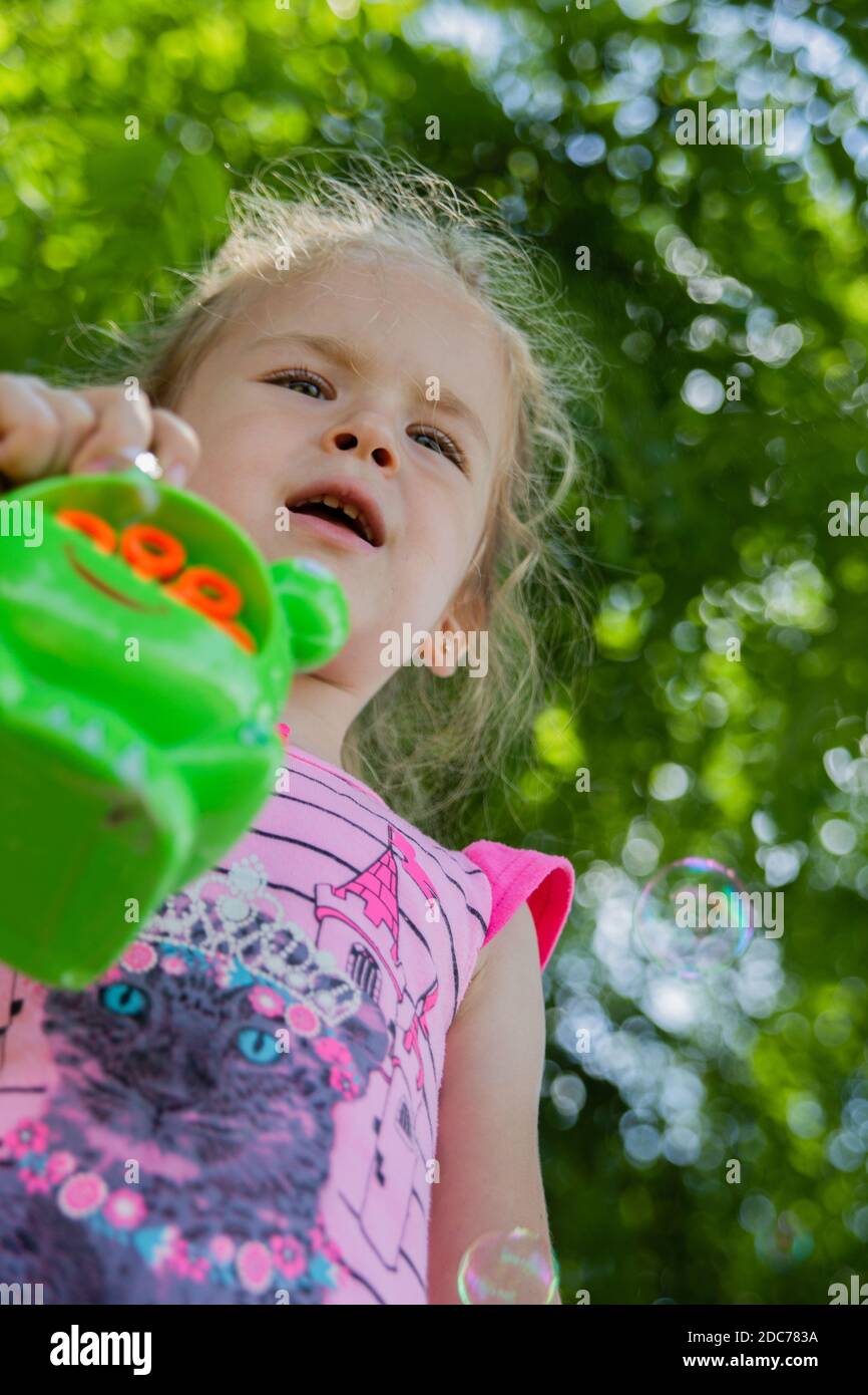 Little blonde girl playing in the park with soap bubbles Stock Photo