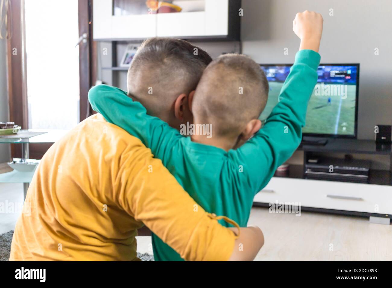 Kids, two boys watching soccer game on television, cheering, holding their arms up in the air Stock Photo