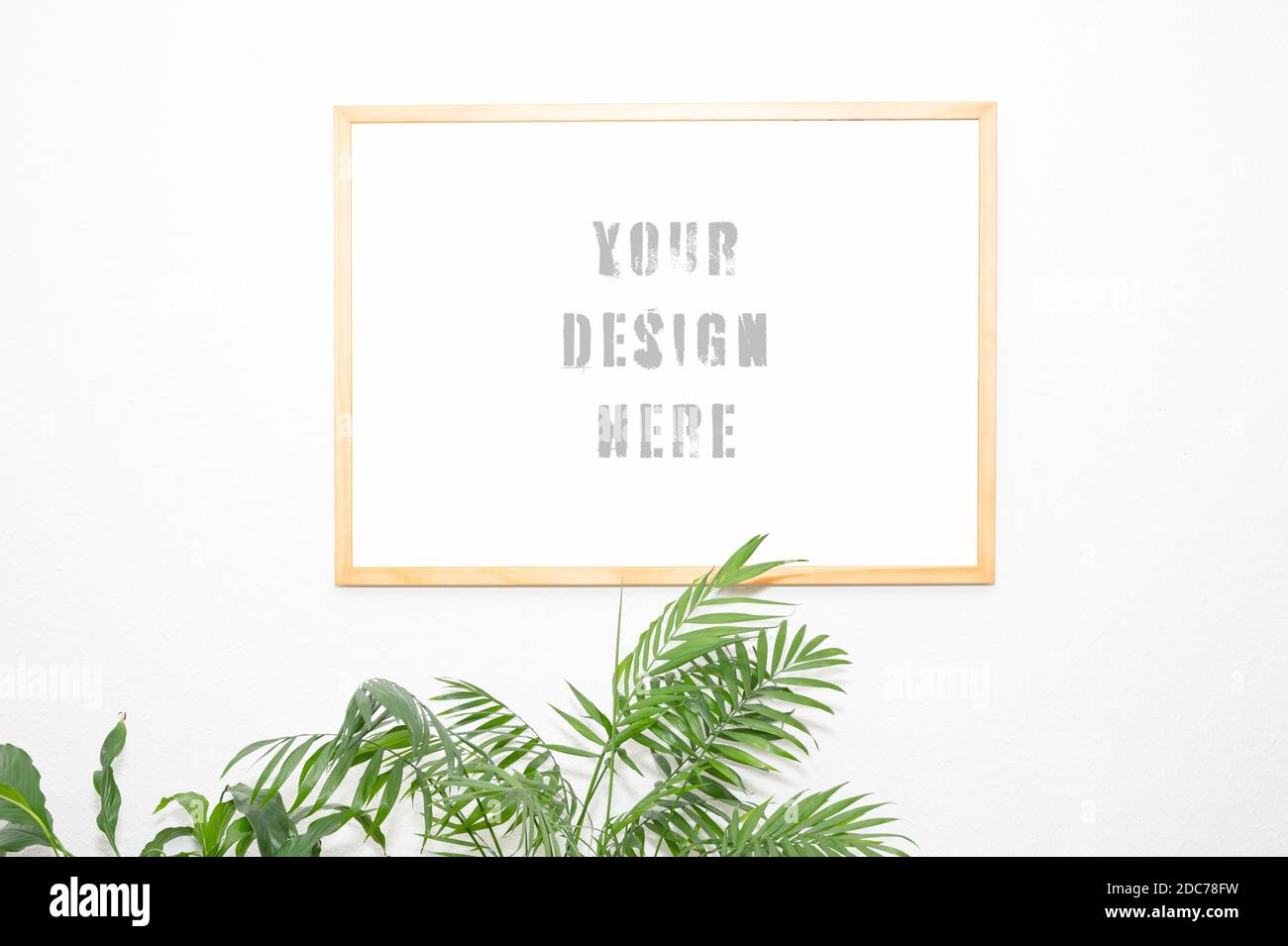 real wood picture frame mockup on a white wall with plants projecting into the picture from below, real photo as design template Stock Photo