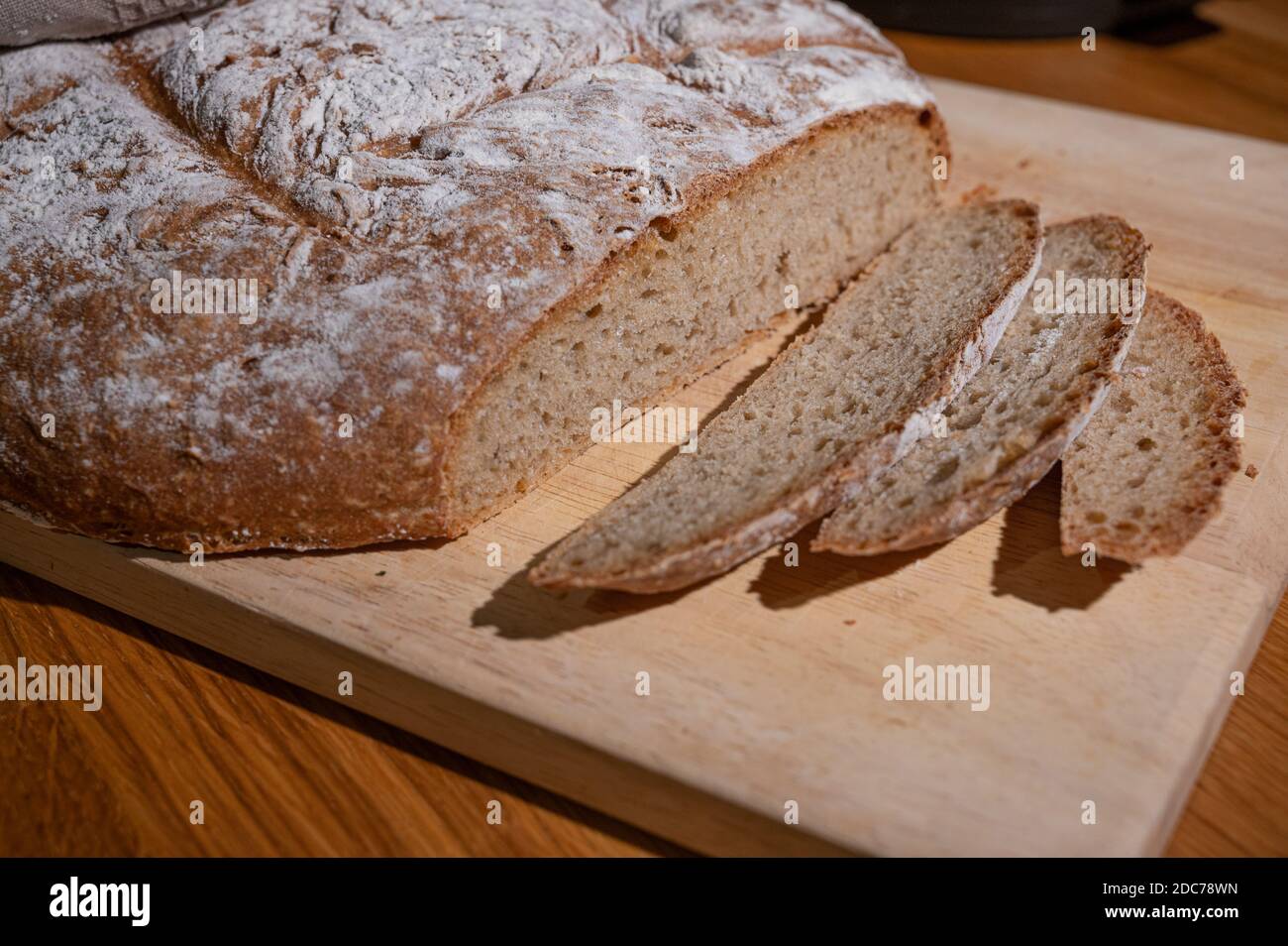fresh farmhouse bread lies wrapped in a cloth on a wooden board and was cut into slices Stock Photo