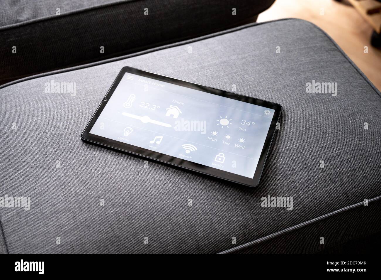 modern smart home control app with flat interface on black tablet display lies on the back of a sofa in front of a blue carpet Stock Photo