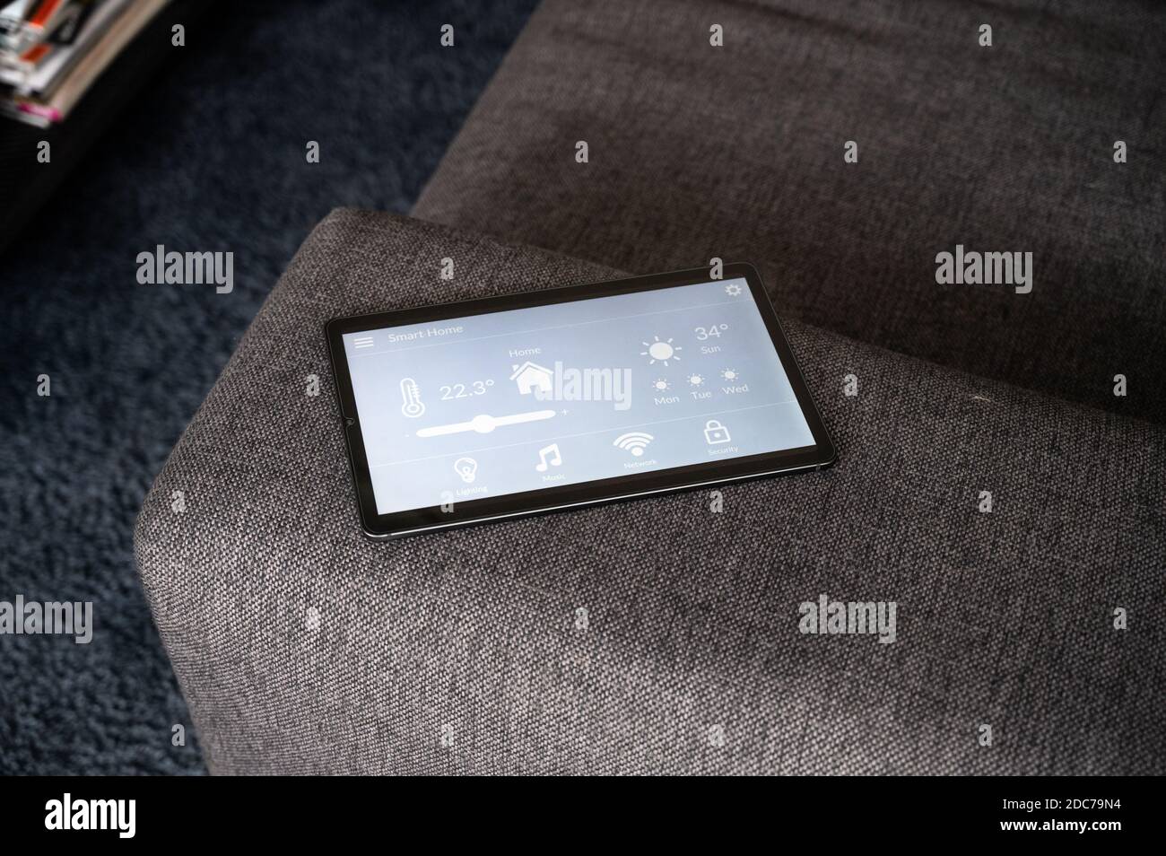 modern smart home control app with flat interface on black tablet display lies on the back of a sofa in front of a blue carpet Stock Photo