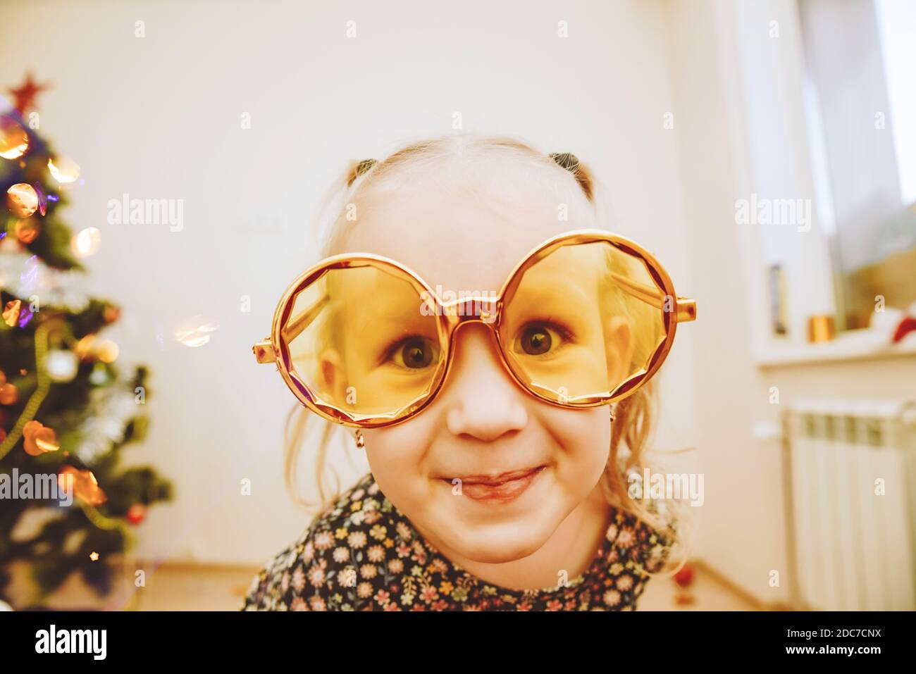Little girl wearing gold masquerade glasses smiling, fooling around. Happy 2021 Stock Photo