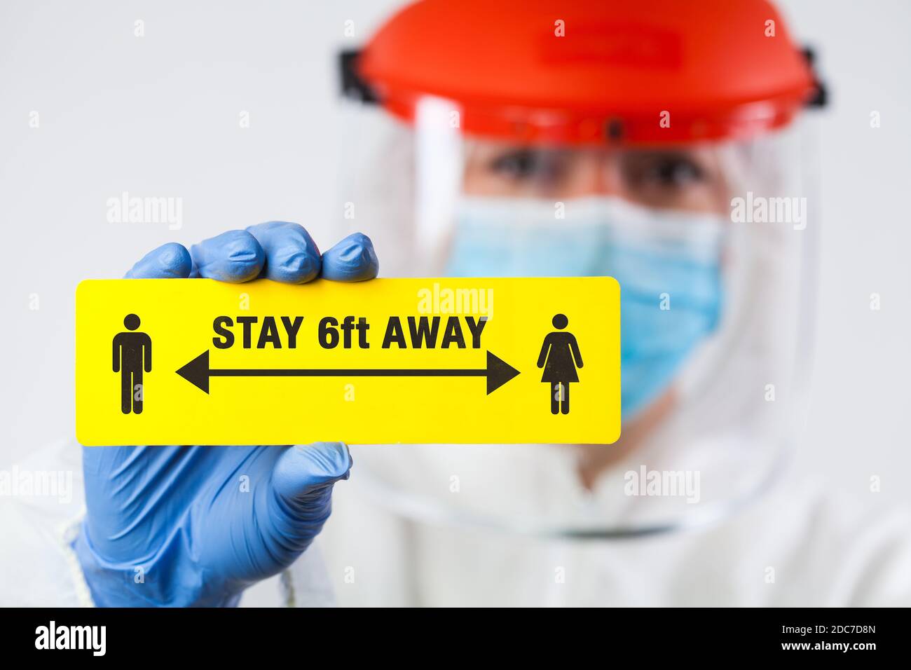 Medical worker in personal protective equipment holding yellow 'STAY 6ft AWAY' sign,social physical distancing to prevent and stop spread of viruses Stock Photo