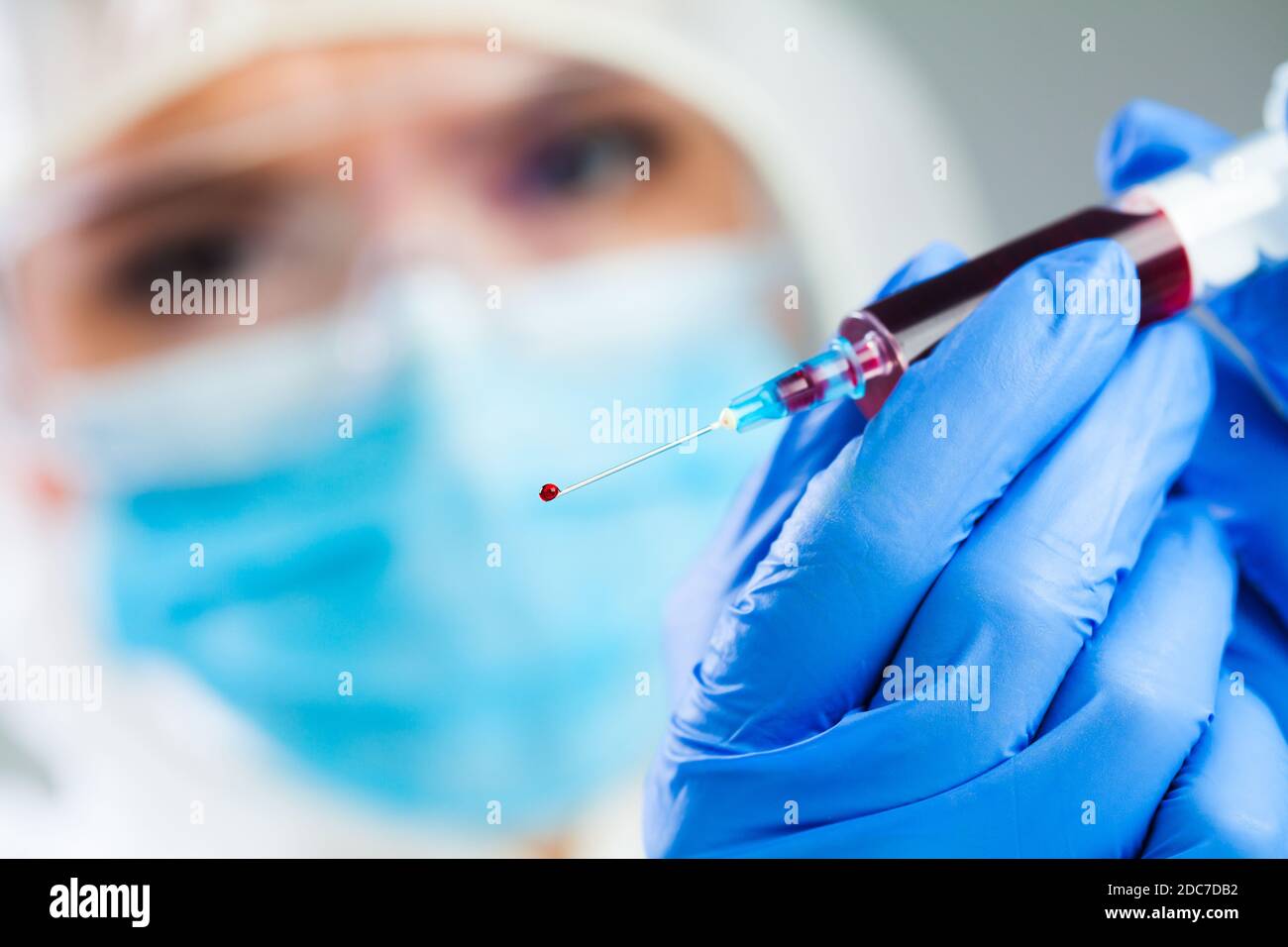 Doctor or lab scientist in personal protective equipment holding syringe full of PRP blood plasma,focus on single drop dripping out of the needle tip Stock Photo
