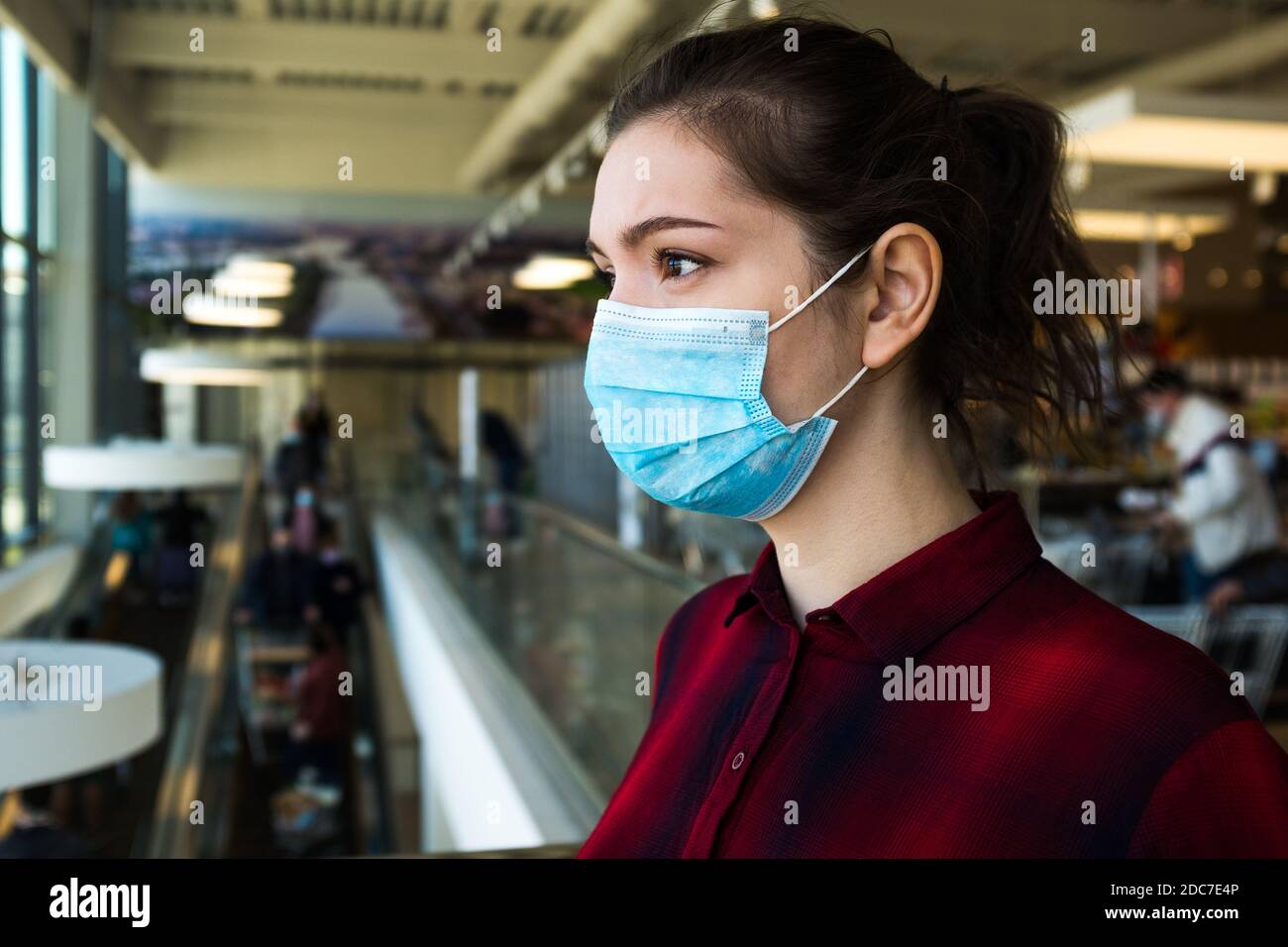 Beautiful pretty worried caucasian young woman wearing protective surgical face mask, standing in a shopping mall or supermarket, stressed and anxious Stock Photo