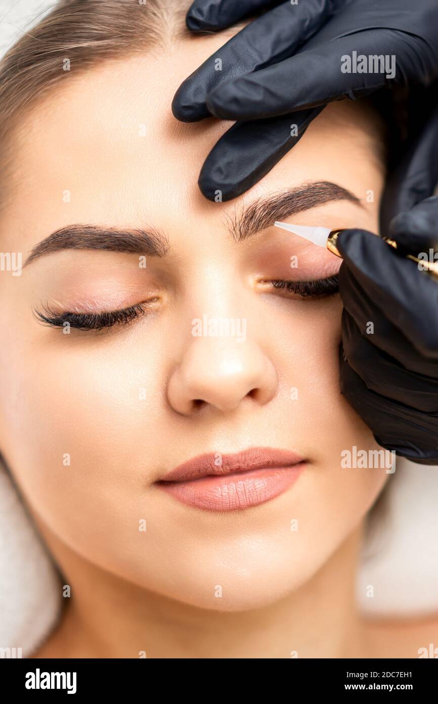 Beautician applying permanent makeup on eyebrows of young woman by special  tattoo machine tool Stock Photo - Alamy