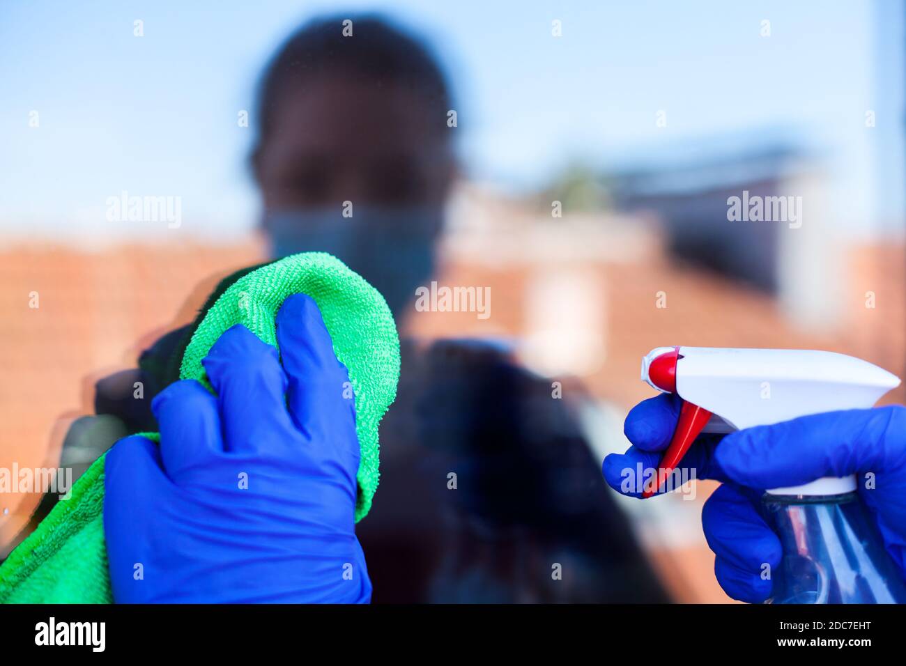Female caucasian person in home isolation cleaning windows with cloth antibacterial sanitizing spray,wearing protective face mask and latex rubber Stock Photo