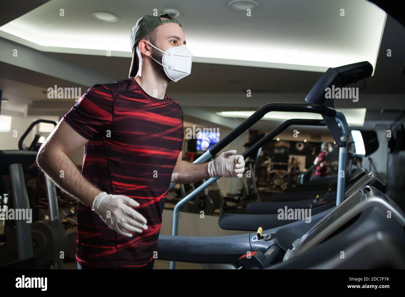 Young man running on treadmill in indoor gym,wearing protective face mask & rubber latex gloves,COVID-19 pandemic prevention of spread & transfer Stock Photo