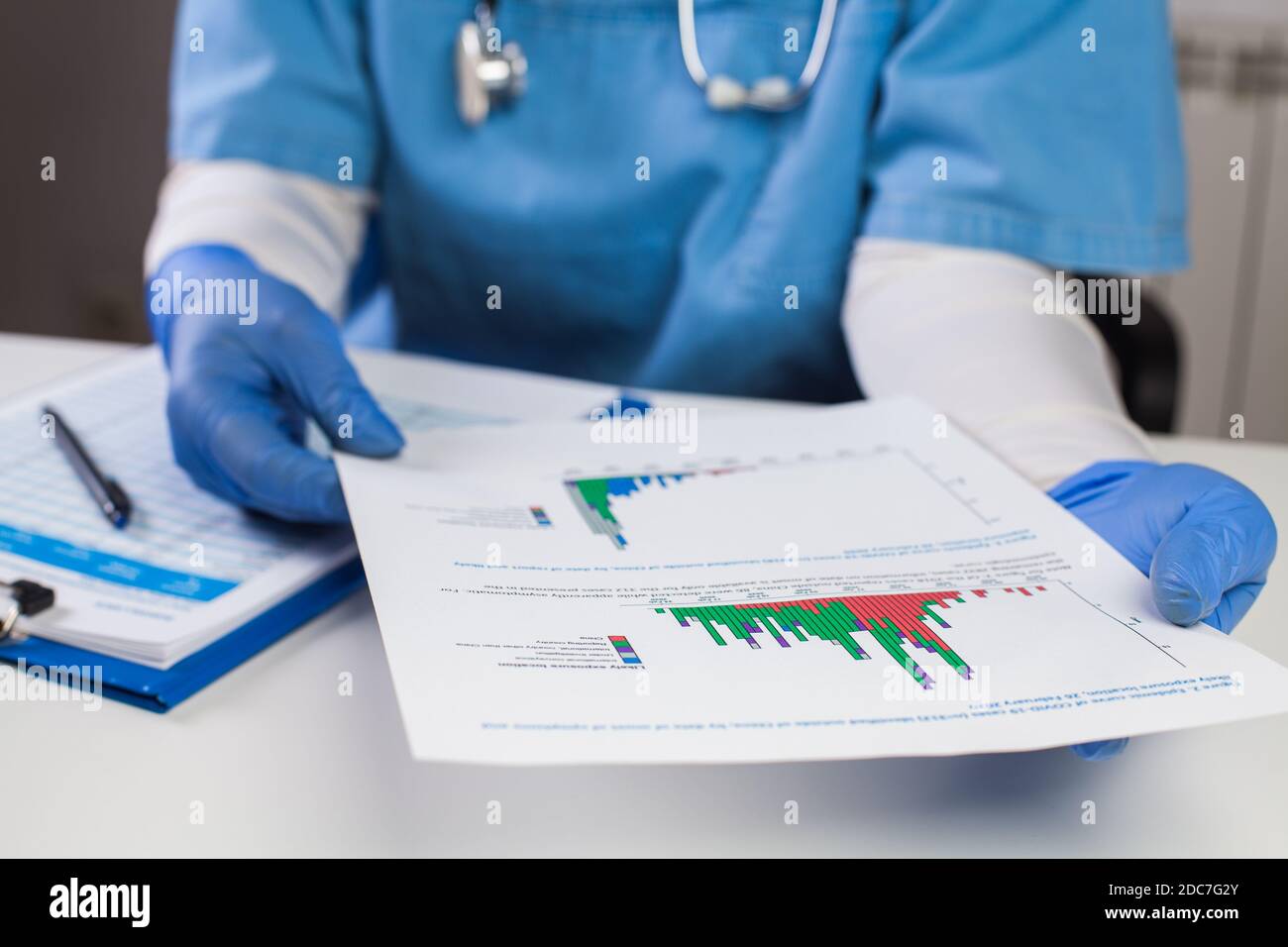 Doctor wearing protective gloves holding document chart,analyzing COVID-19 graph data,Coronavirus global pandemic outbreak crisis,stats showing number Stock Photo