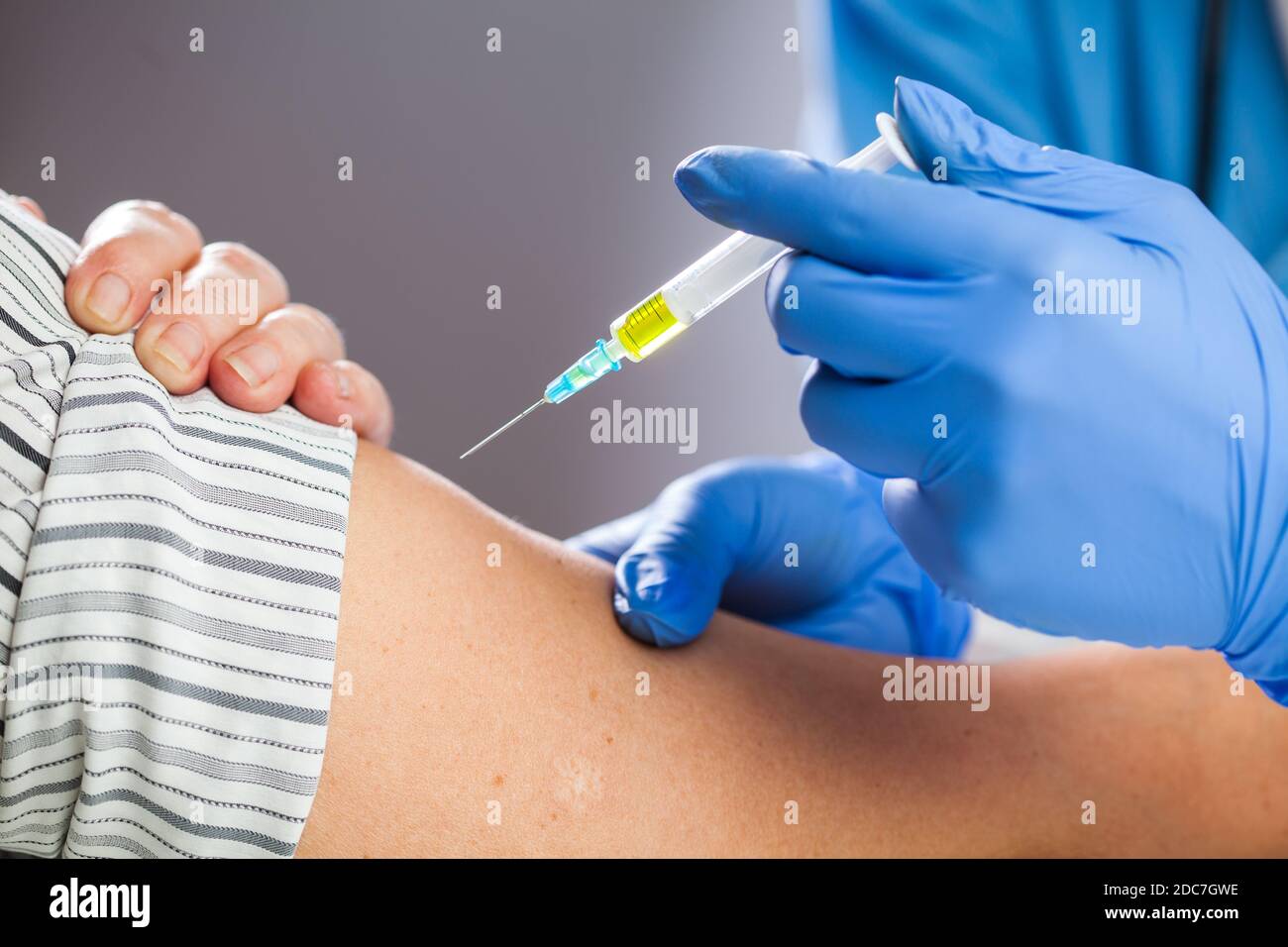 Coronavirus COVID-19 immunisation concept,medical worker wearing blue protective latex gloves holding syringe filled with yellow liquid,giving patient Stock Photo
