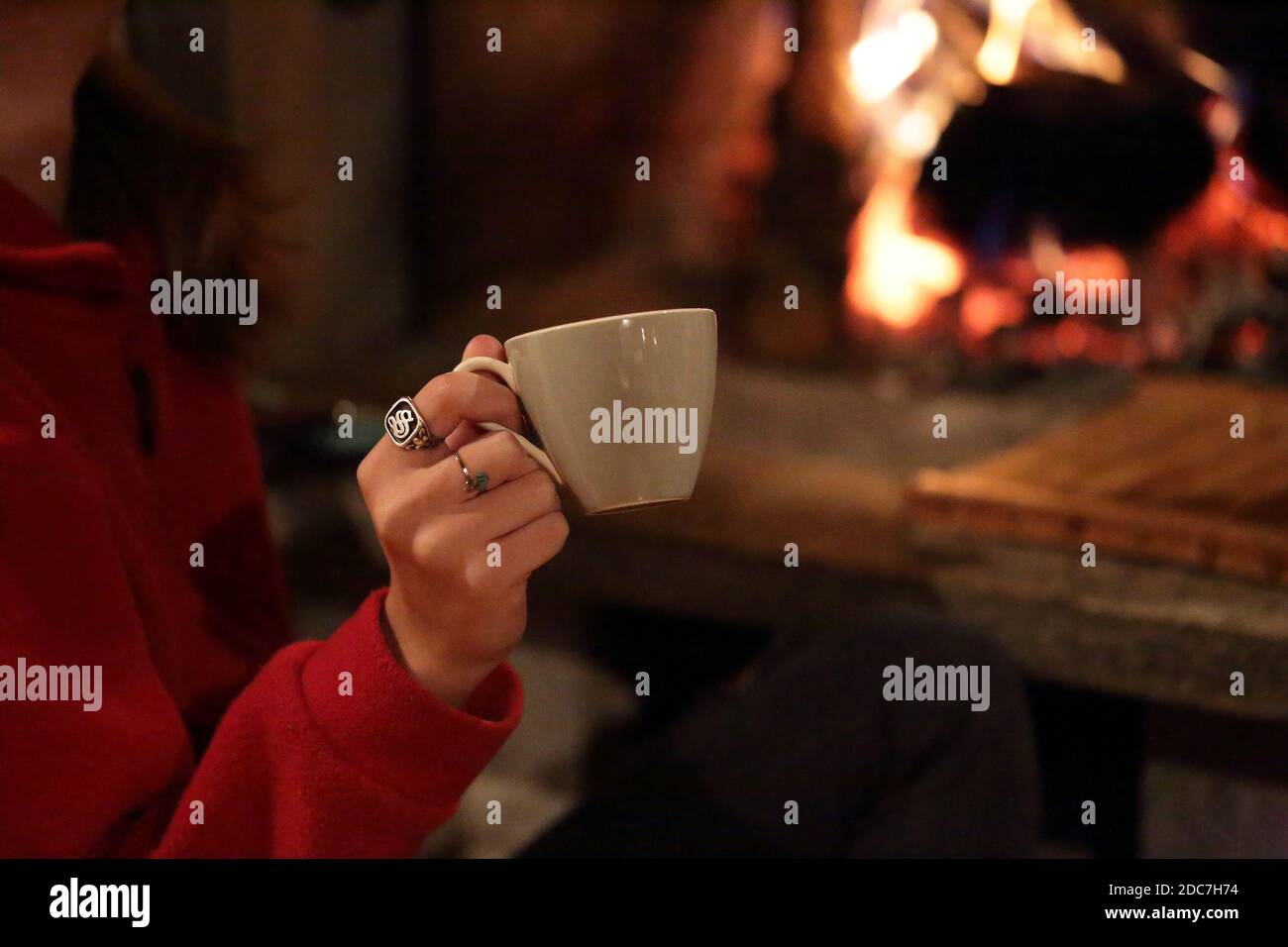 Girl's hand holding a cup with fireplace in the background Stock Photo