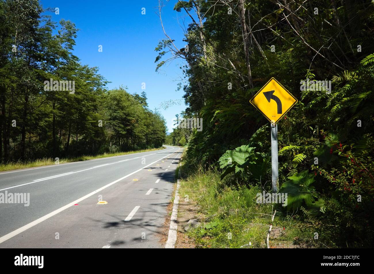 Turn right road sign along the empty highway road in Chile. Warning road sign with black arrow on yellow background along bicycle lane. Stock Photo