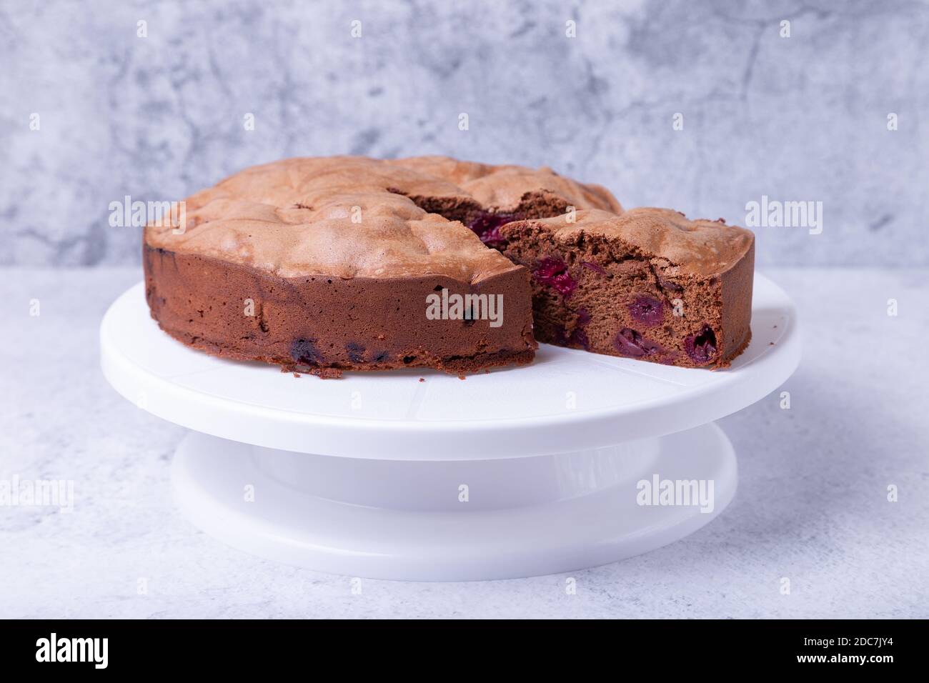 Chocolate pie with cherries on a white cake stand, one piece cut off. Homemade baking. Close-up. Stock Photo