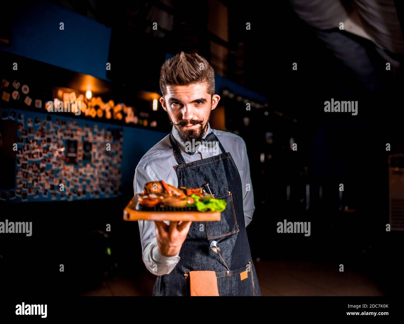 Professional friendly waiter serves appetizing dish on a black background. Stock Photo