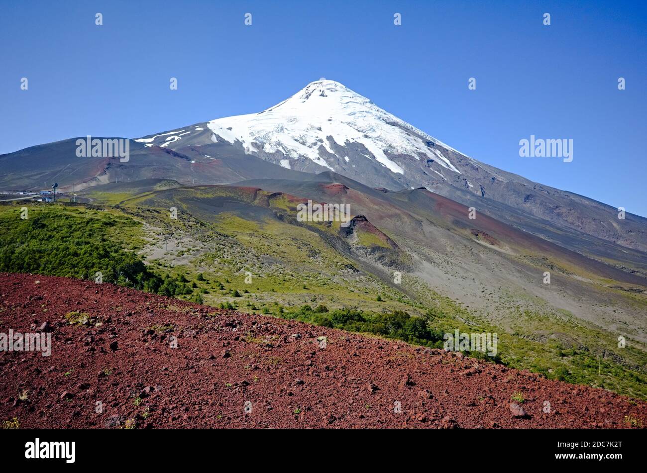 Osorno Volcano view from the crater on slopes with beautiful colors of red, green and snow capped volcano peak and clear blue sky. Stock Photo