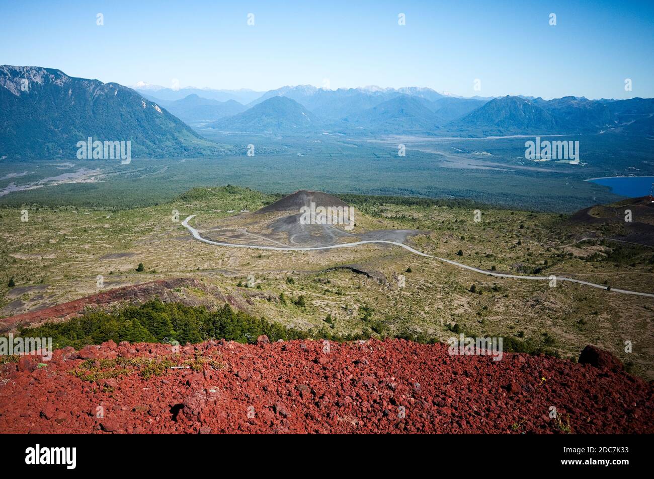 Aerial view to a valley with curved road to mountains. Foothills of Osorno Volcano. Red volcanic rocks on foreground. Osorno, Puerto Varas, Chile Stock Photo