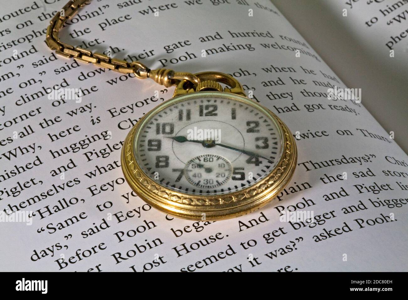 A man's gold pocket watch and chain lying on a copy of Winnie the Pooh. Stock Photo