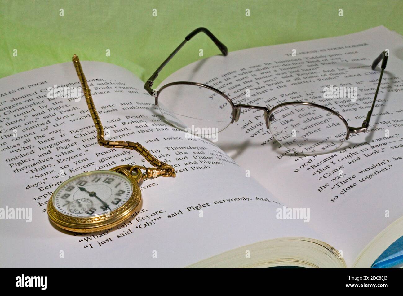 A man's gold pocket watch and chain lying on a copy of Winnie the Pooh. Stock Photo