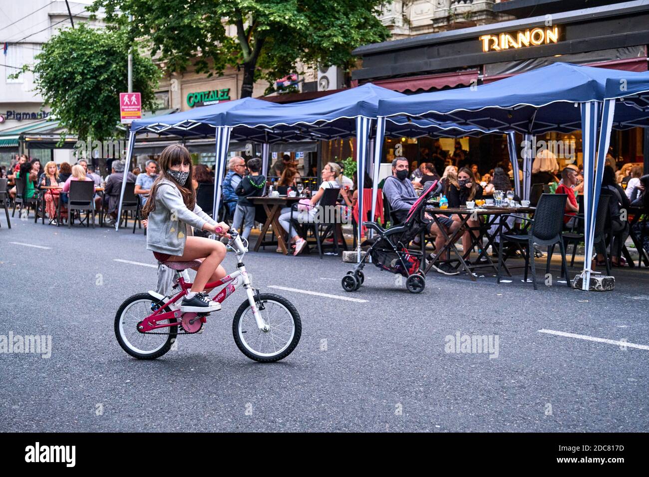 Buenos aires / Argentina; Nov 14, 2020: Girl riding a bike with a protective face mask, and people eating outdoors. New normalcy during the coronaviru Stock Photo