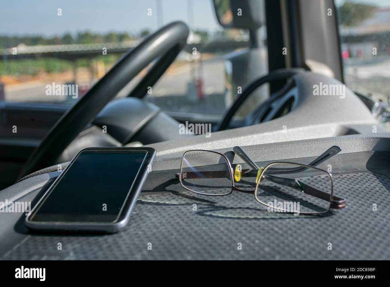 Glasses and mobile phone on the dashboard of a truck. Stock Photo
