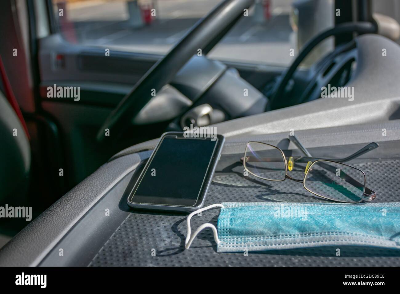 Surgical mask, glasses and mobile phone on the dashboard of a truck. Stock Photo