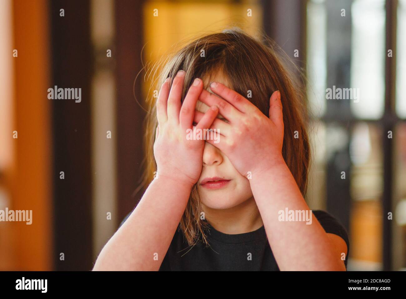 Close-up of a small child hiding behind her hands Stock Photo