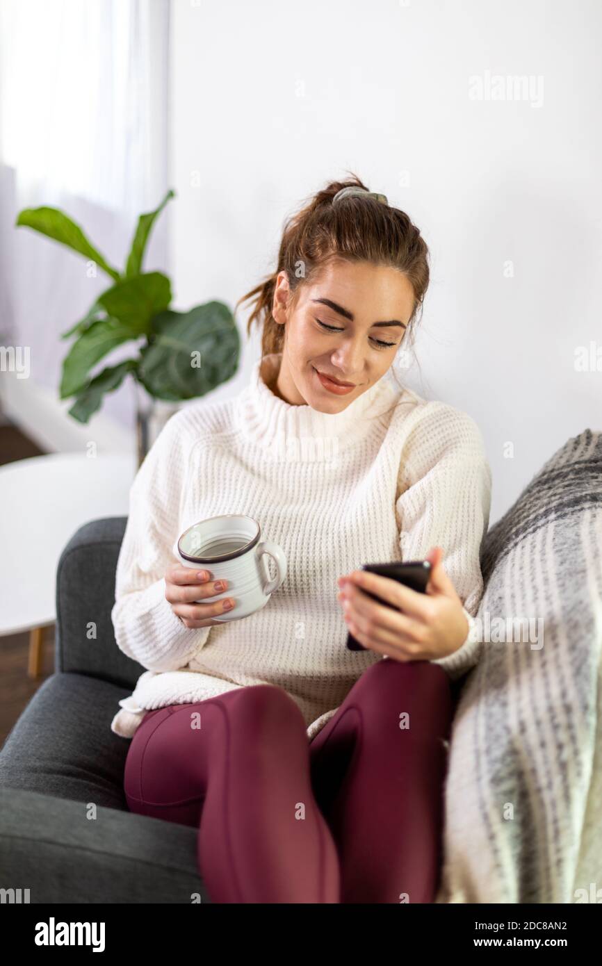 Woman holds mug while checking her phone Stock Photo