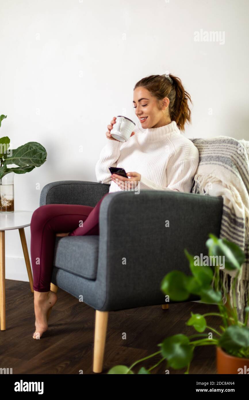Woman holds mug while checking her phone Stock Photo