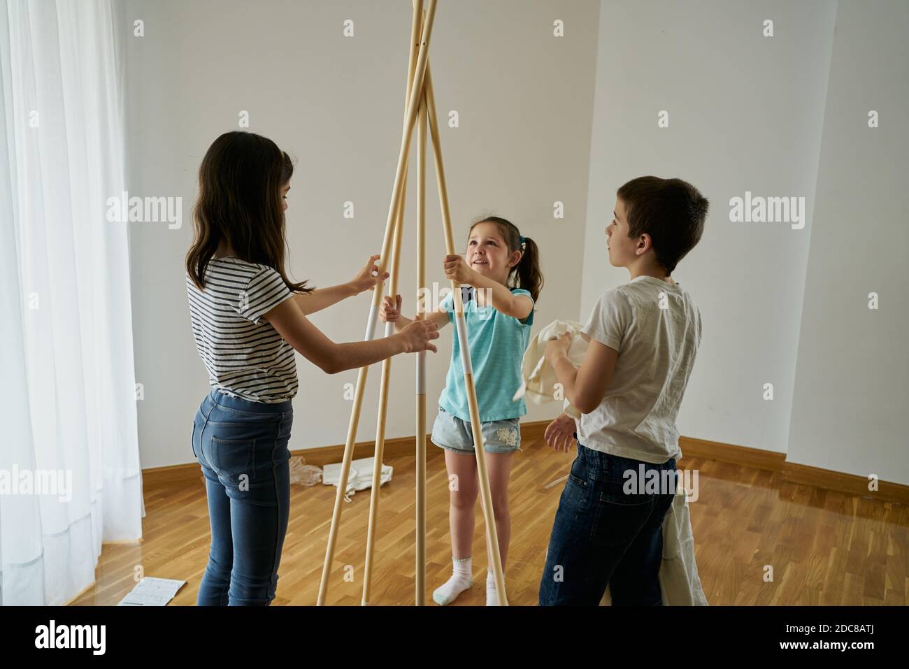 Children putting the sticks to build a teepee tent inside their house