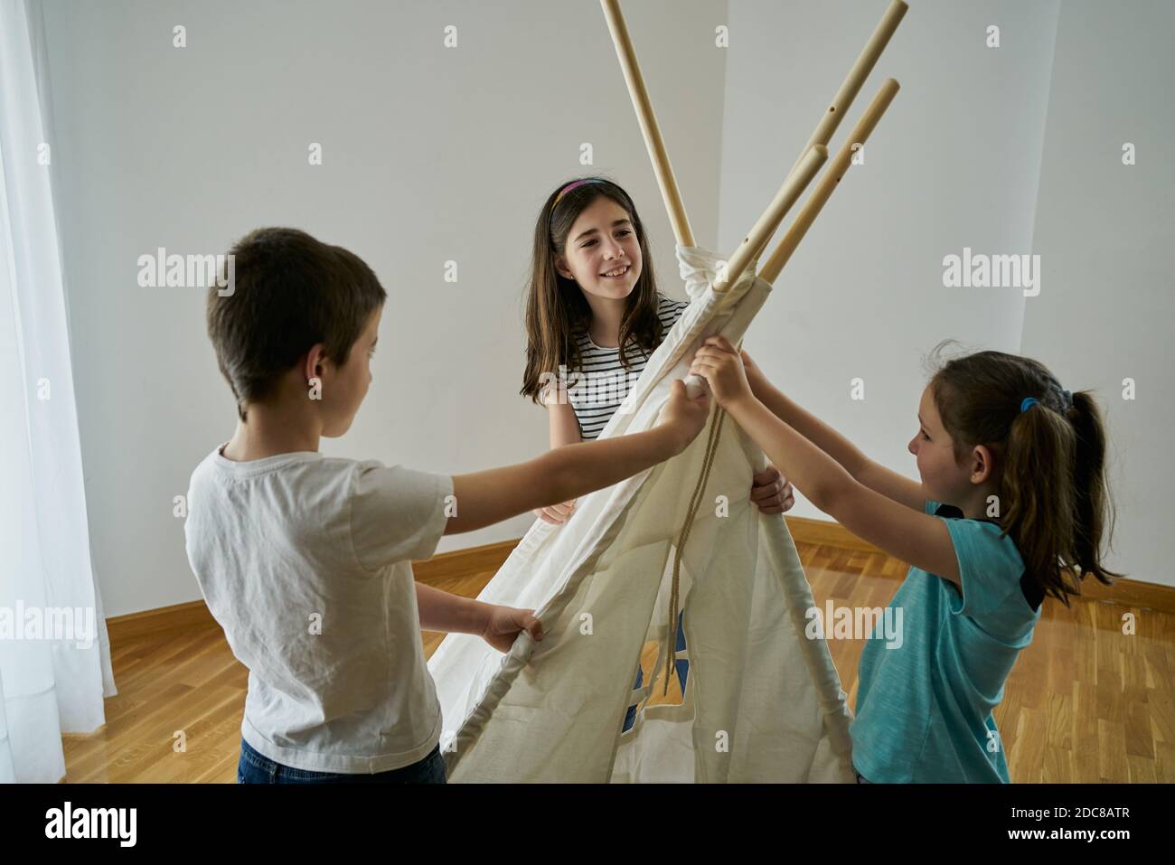 Children putting the sticks to build a teepee tent inside their house