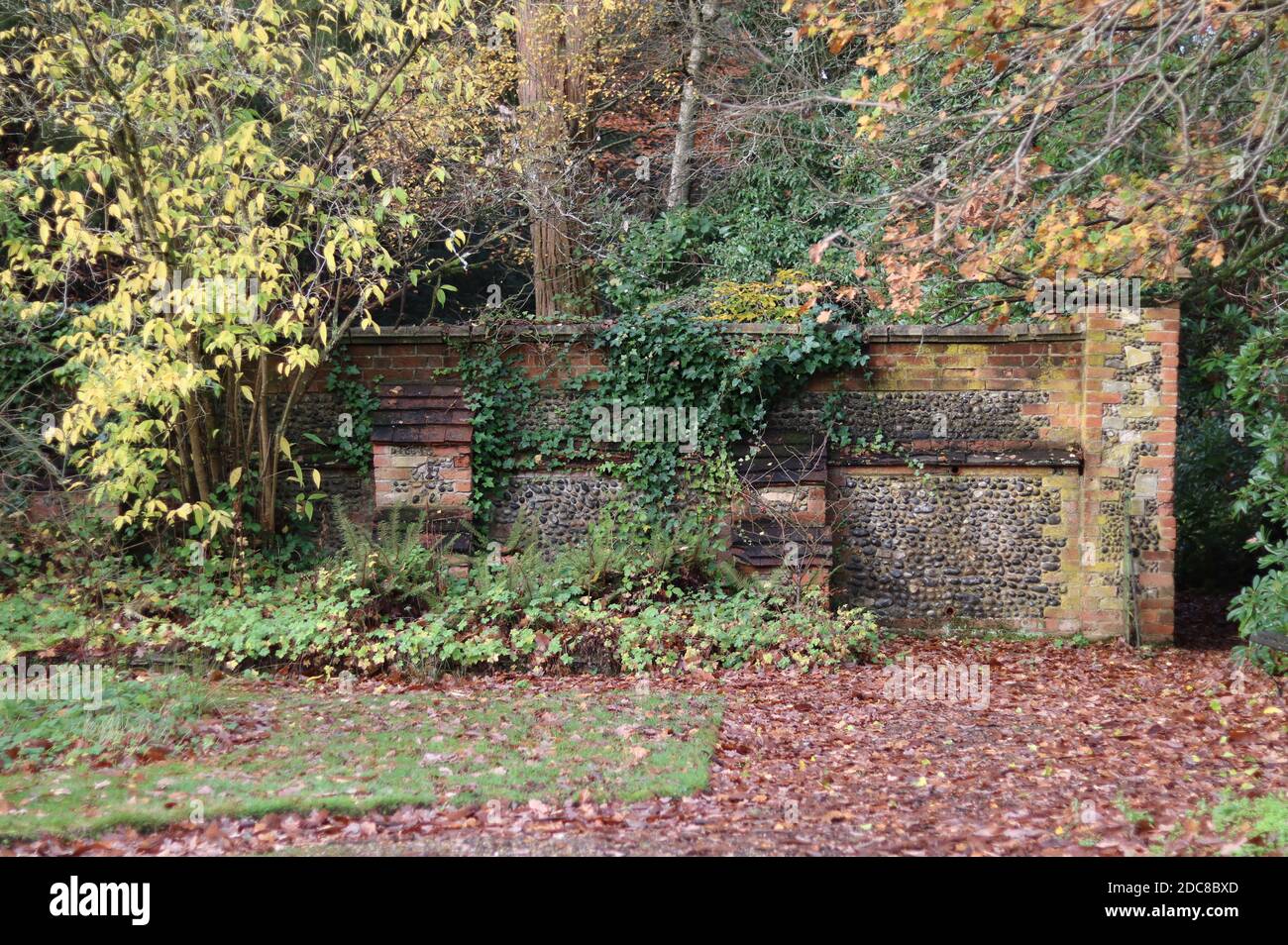 Image of very old stone and brick wall in autumn with yellowing trees and bushes Stock Photo