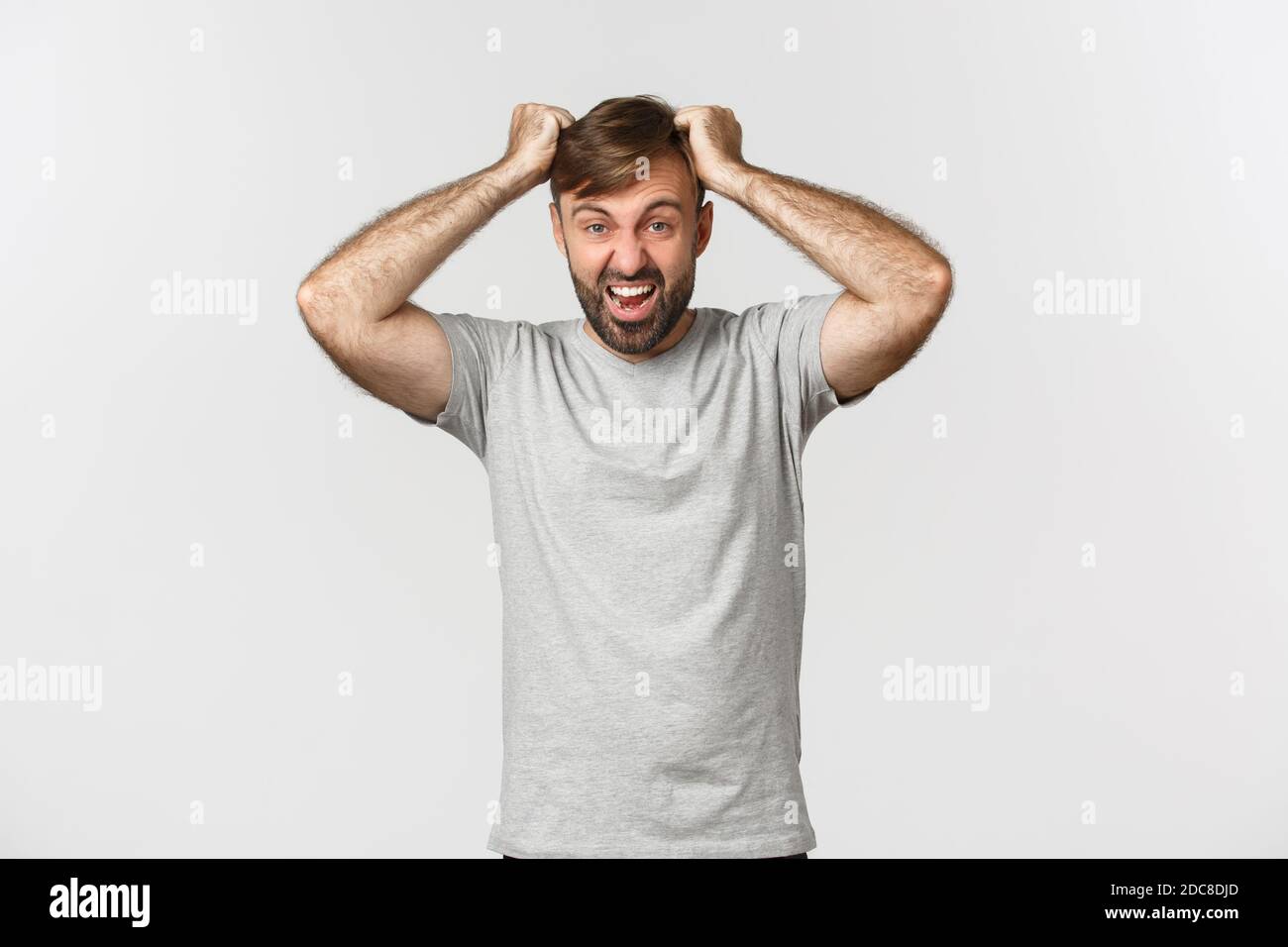 Portrait of distressed mad guy in gray t-shirt, ripping hair from anger and shouting, standing over white background Stock Photo