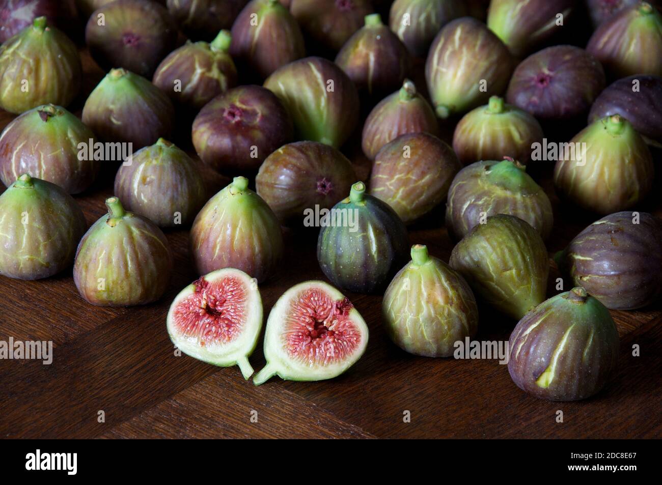 A freshly picked fig “Ficus carica” cut in half to reveal the seeds and succulent red flesh. Against a background of figs laid out on a wooden table. Stock Photo