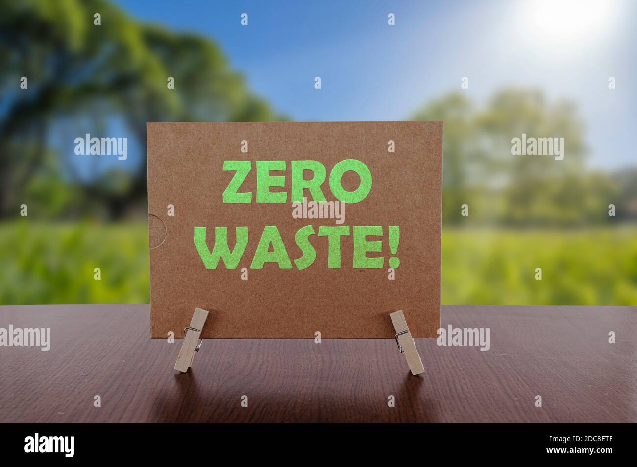 Zero waste text on card on the table with sunny green park background. Ecology concept, recycle, reuse, reduce waste. Stock Photo