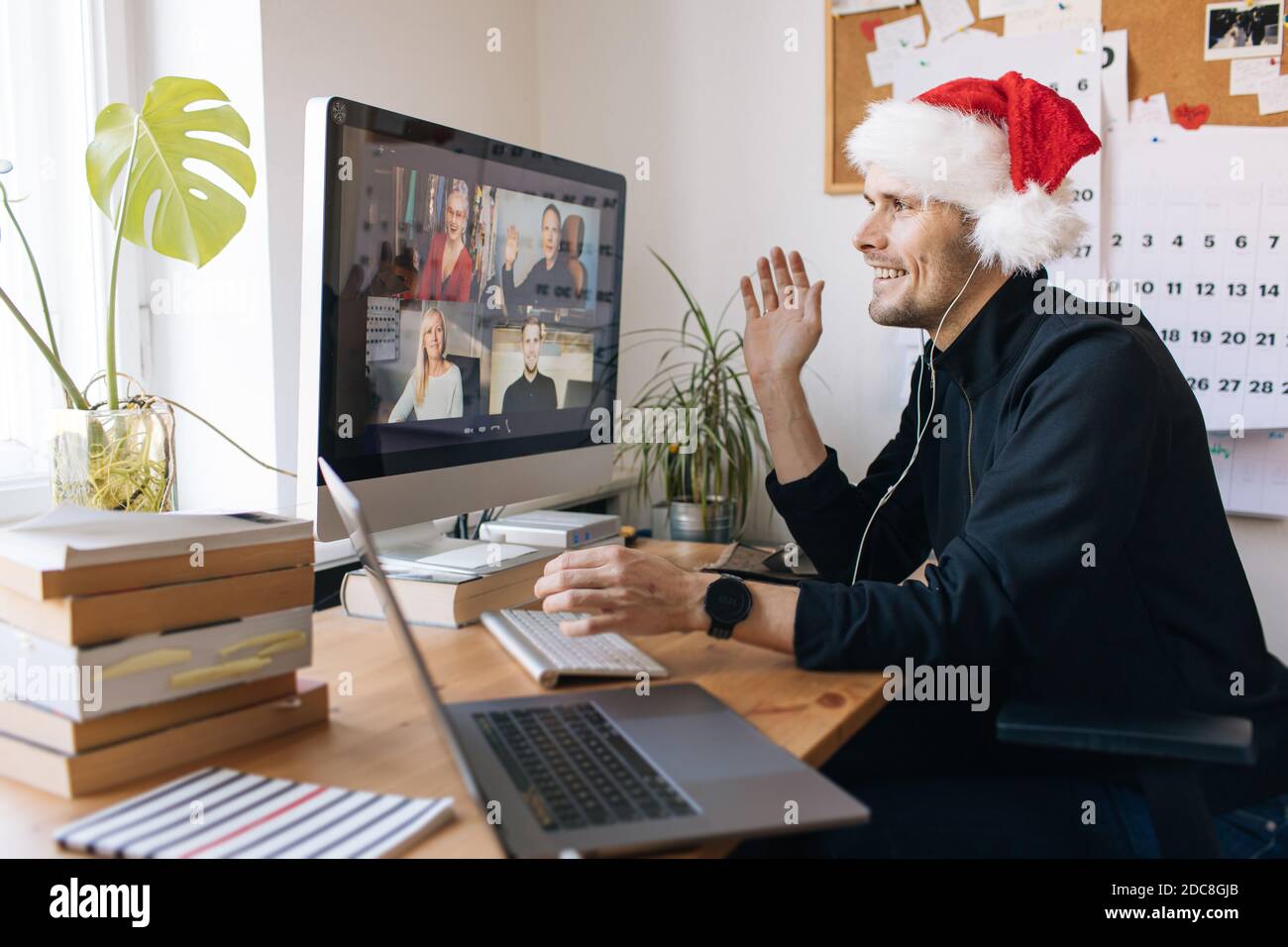 Virtual Christmas day house party. Man smiling wearing Santa hat Business video conferencing Young man having video call via computer in the home xmas Stock Photo