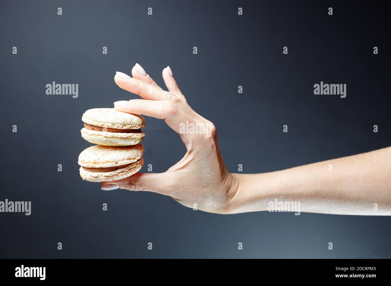 The female hand holds holding colorful French macarons. Delicious dessert on dark grey background Stock Photo