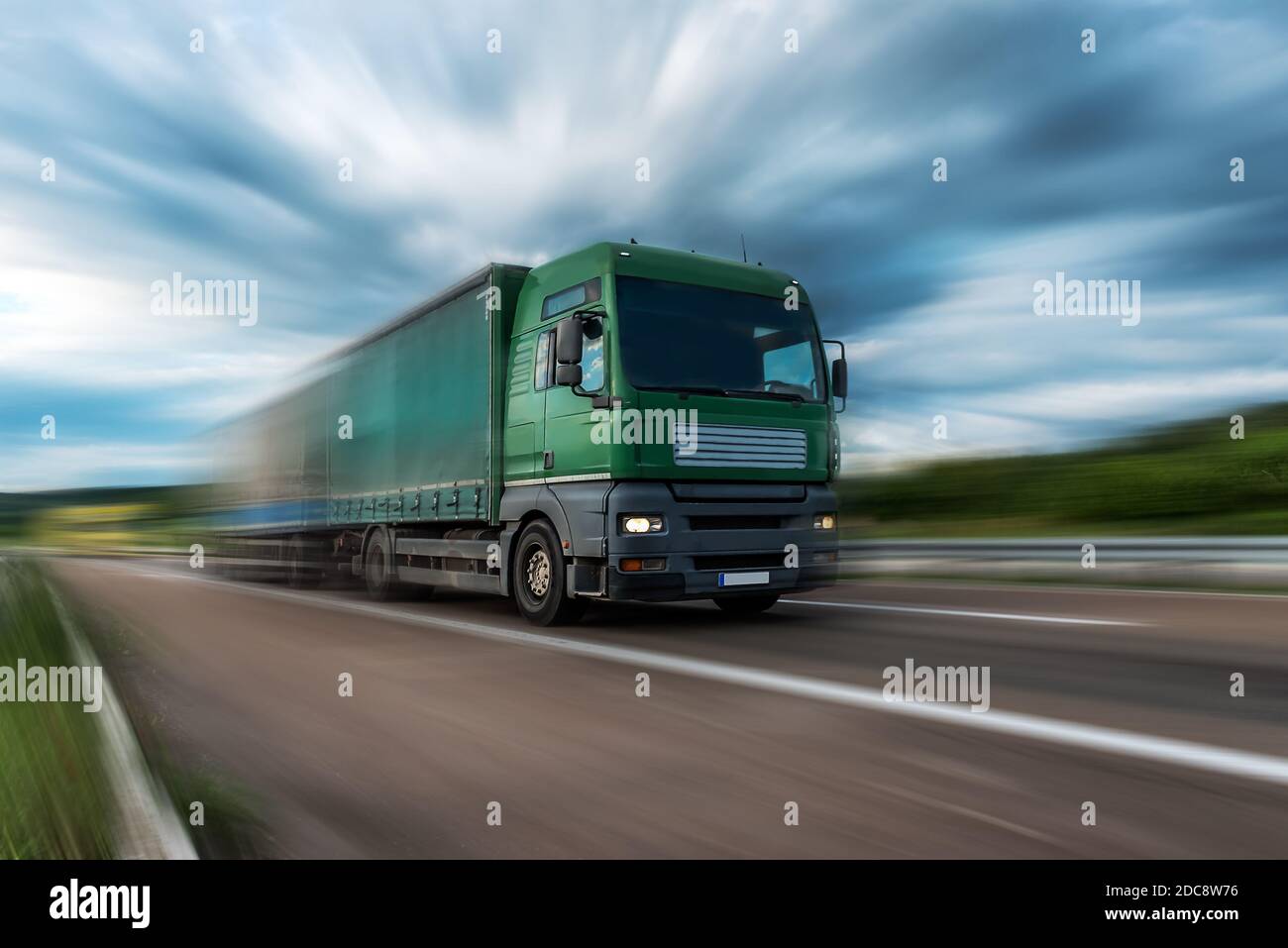 Green Lorry truck speeding on freeway at sunset, motion blurred Stock
