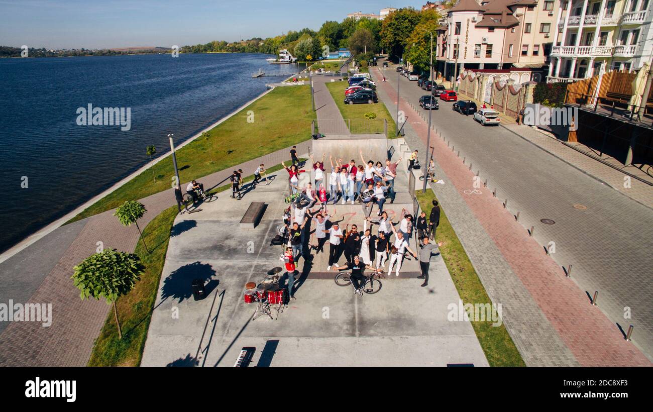 Aerial view of happy youth with musical instruments in a skate park on the embankment. Surreal storyline. Stock Photo