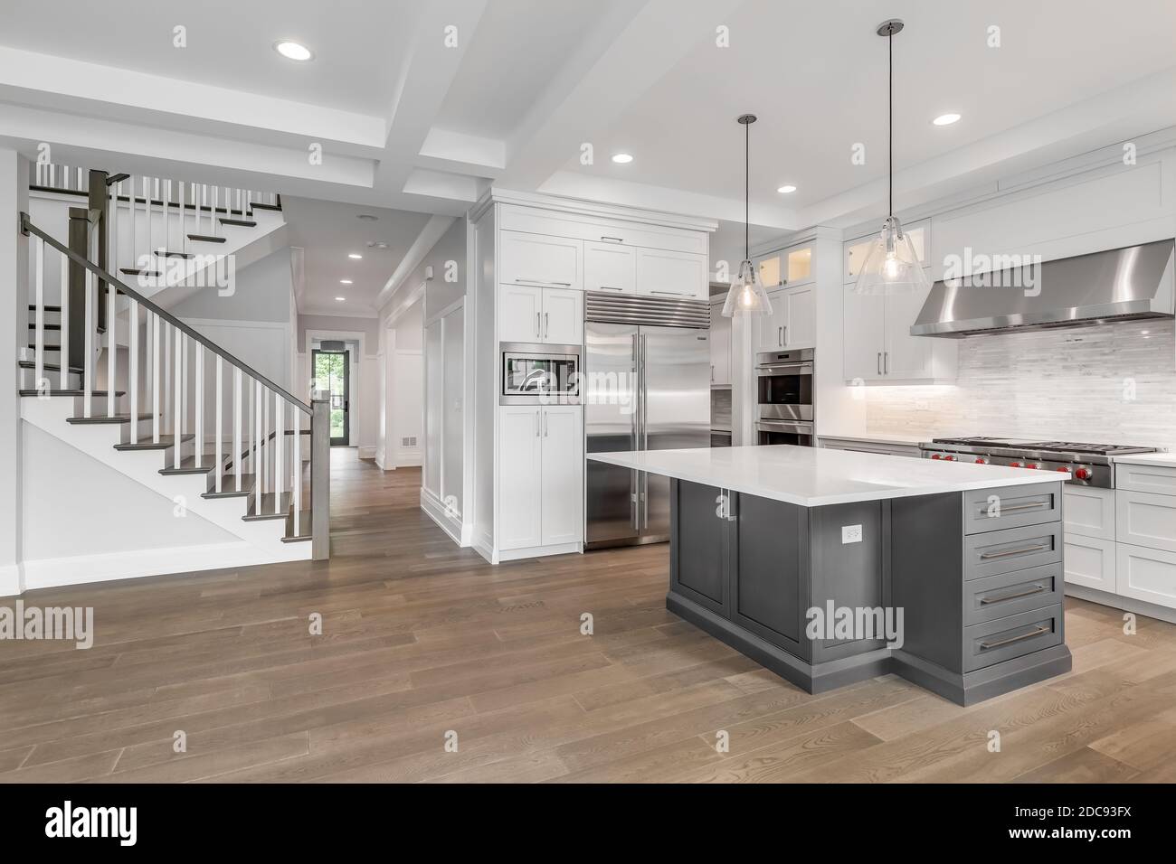 A Luxury Home With A White Kitchen Featuring A Grey Island And Stainless Steel Appliances Looking Towards A Staircase And Hallway To The Entryway Stock Photo Alamy