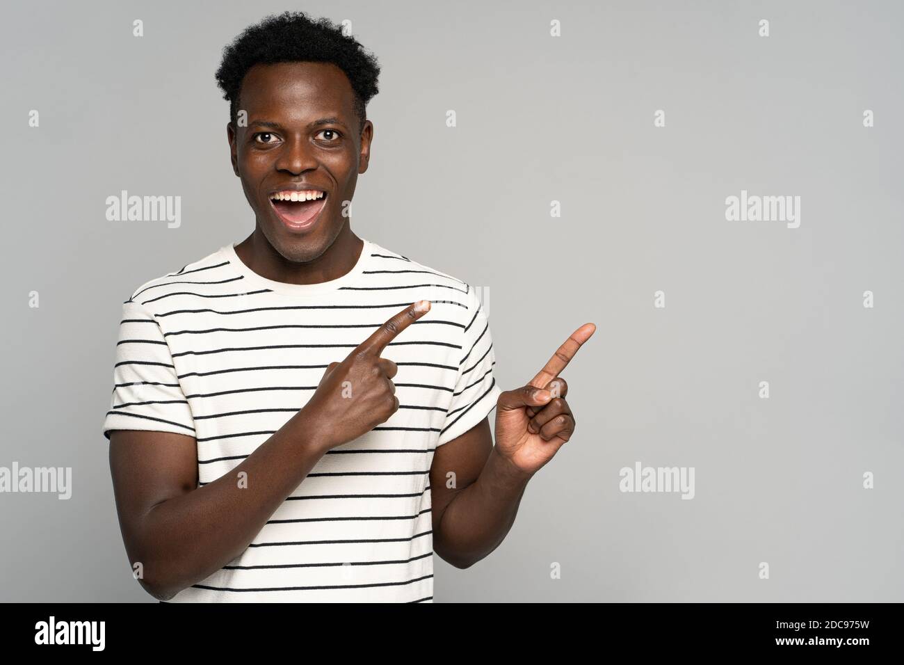 Laughing Black man in stripped t-shirt points away with fingers, look at camera, showing blank copy space for advertising, offering, product, promotio Stock Photo