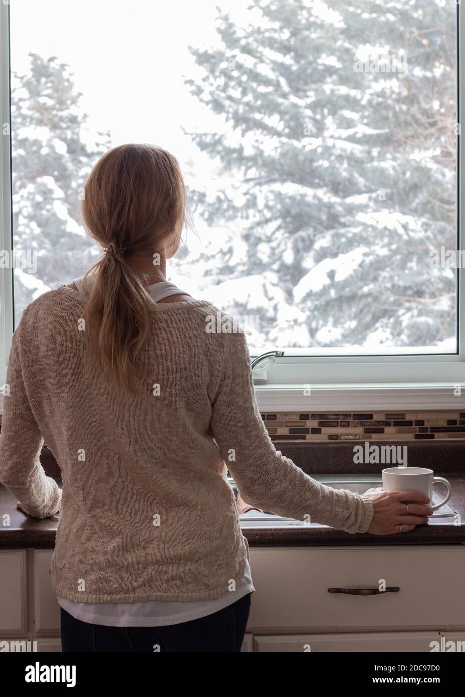 Portrait of motherhood, woman looking out window in kitchen with coffee in hand Stock Photo