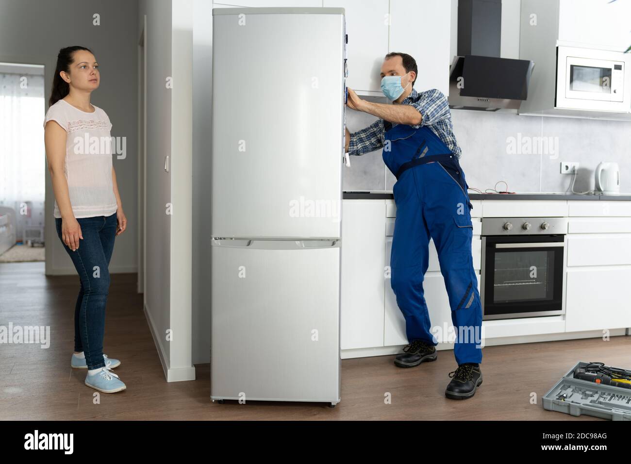 Fridge Handyman Service In Face Mask. Broken Refrigerator Stock Photo