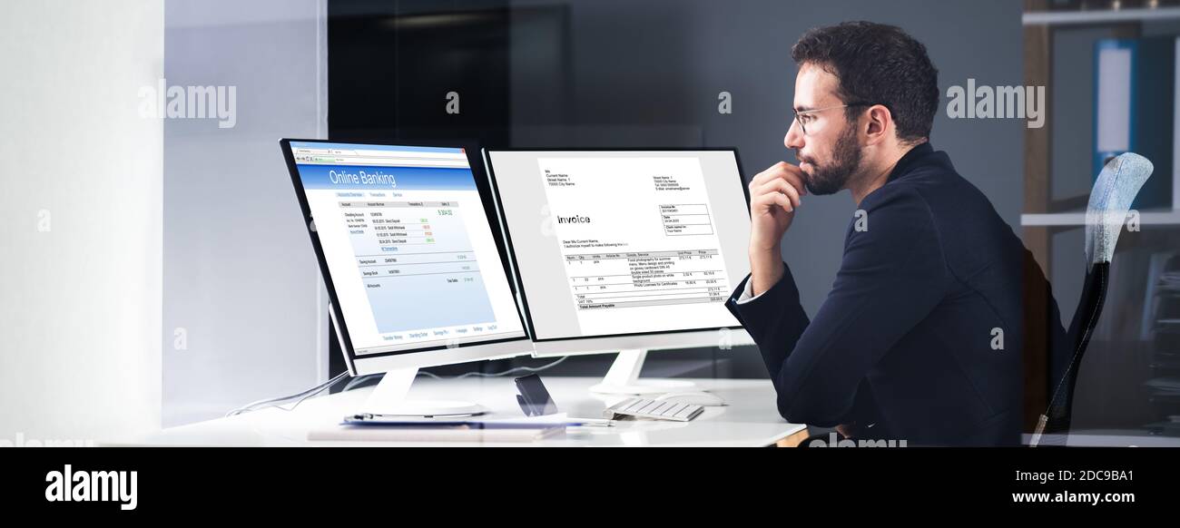 Young Businessman Looking At Invoice While Doing Online Banking On Computer Stock Photo