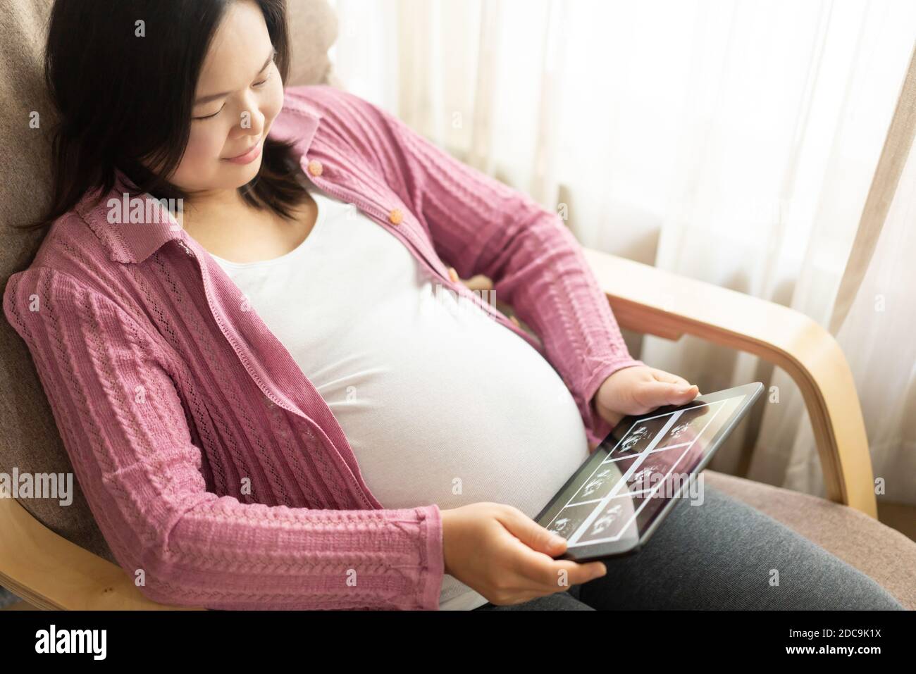 Pregnant woman feeling happy at home while taking care of her child. The young expecting mother holding baby in pregnant belly. Maternity prenatal Stock Photo