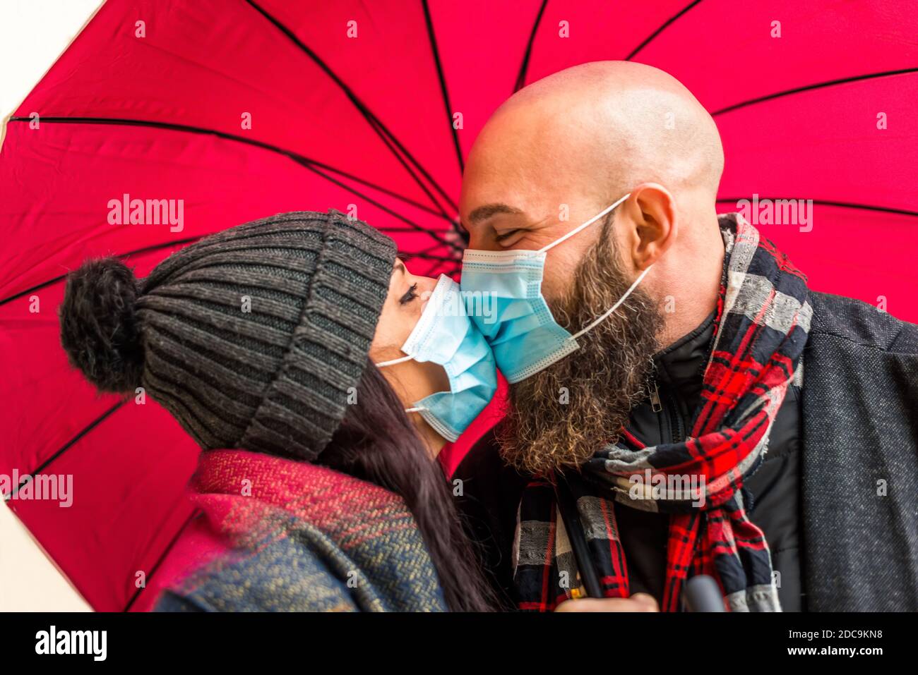 isolated close up portrait of a young adult couple kissing each other with passion wearing protective face mask.hipster man and caucasian woman Stock Photo
