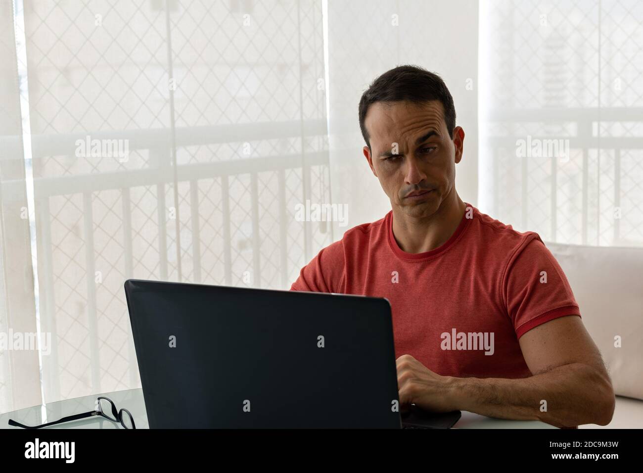 Mature man working at home and looking with suspicious face to the laptop screen. Stock Photo